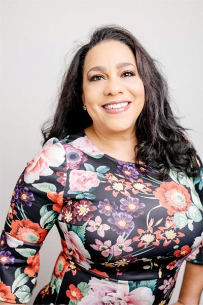 A woman in floral print shirt smiling for the camera.